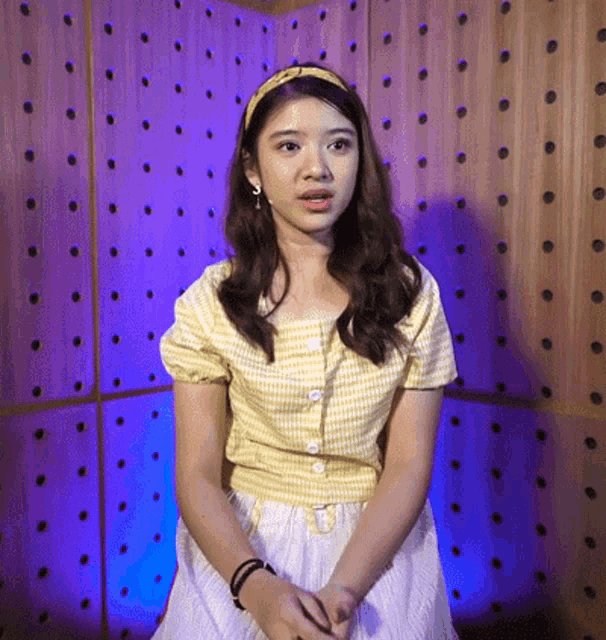 a woman in a yellow shirt and white skirt is standing in front of a wooden wall with holes in it