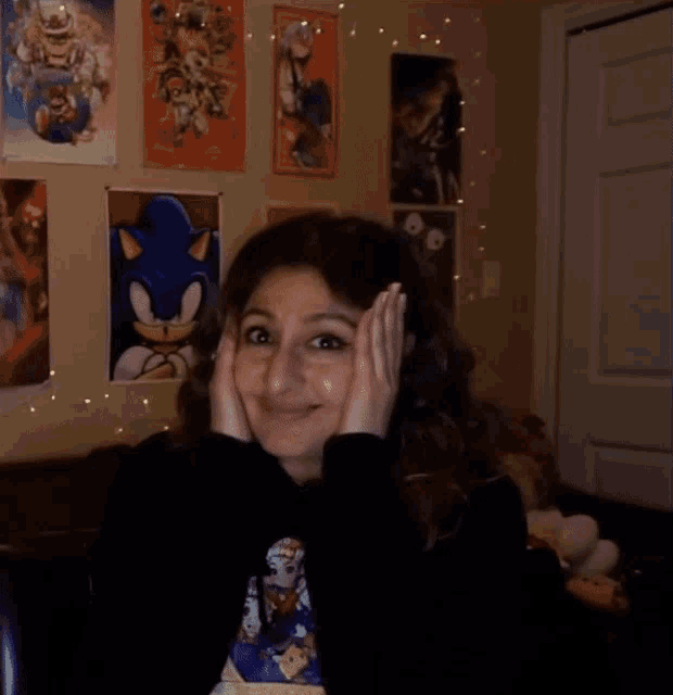 a woman wearing a sonic the hedgehog t-shirt smiles with her hands on her face