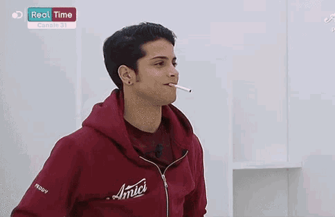 a man smoking a cigarette while wearing a red hoodie that says amici