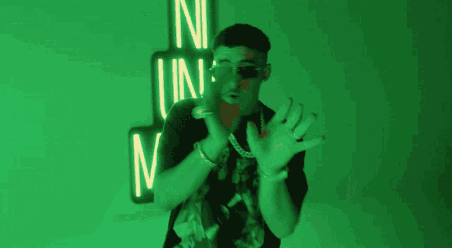 a man in sunglasses stands in front of a neon sign that says n una os