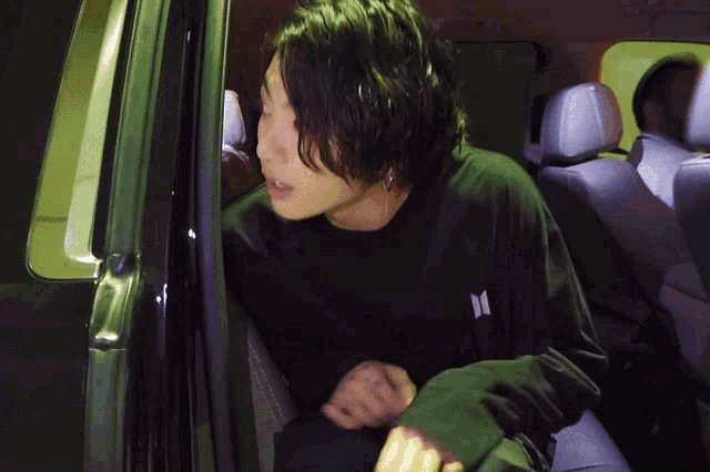 a man in a black shirt with the letter m on it is sitting in the back seat of a car