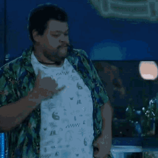 a man in a hawaiian shirt is pointing to his chest