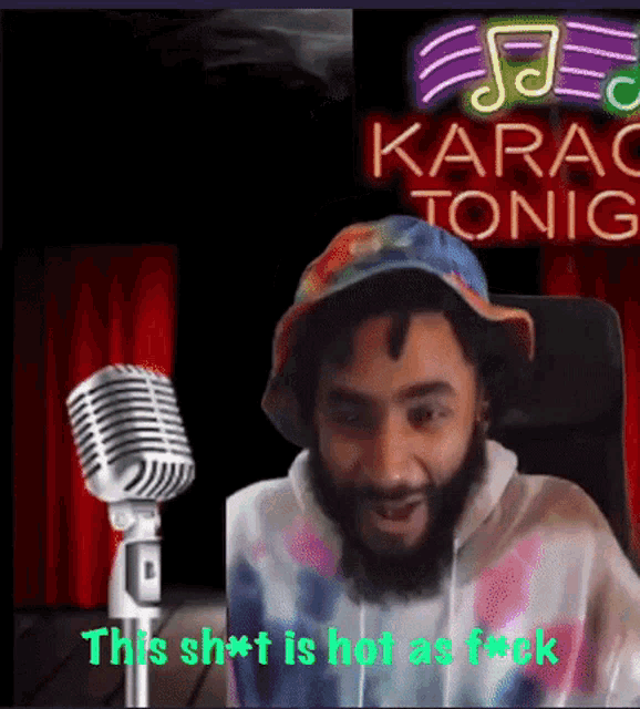a man wearing a tie dye hat is sitting in front of a microphone and a sign that says karao tonic