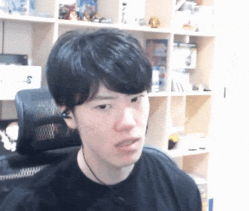 a man wearing a black shirt and ear buds is sitting in front of a bookshelf