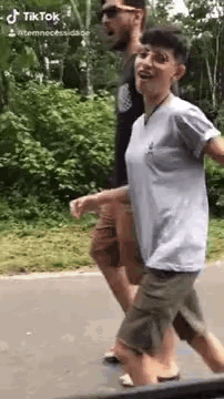 a man and a woman are walking down a street . the woman is wearing glasses and a gray shirt .