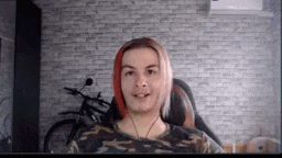 a man with red hair is sitting in a chair in front of a brick wall and a motorcycle .