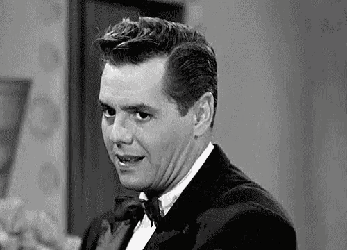 a man in a tuxedo and bow tie is looking at the camera in a black and white photo .
