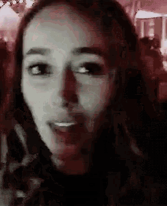 a close up of a woman 's face in a dark room with a crowd in the background .