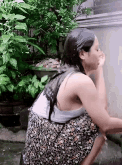 a woman in a floral skirt is kneeling down in front of a wall .