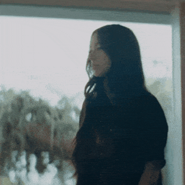 a woman with long hair looks out a window
