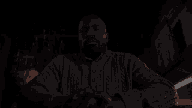 a man with a beard is sitting in a dark room looking at the camera .