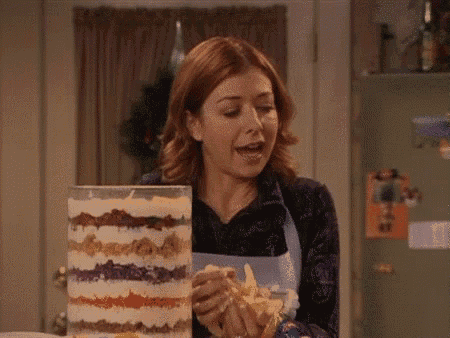 a woman in an apron is looking at a trifle in a glass container