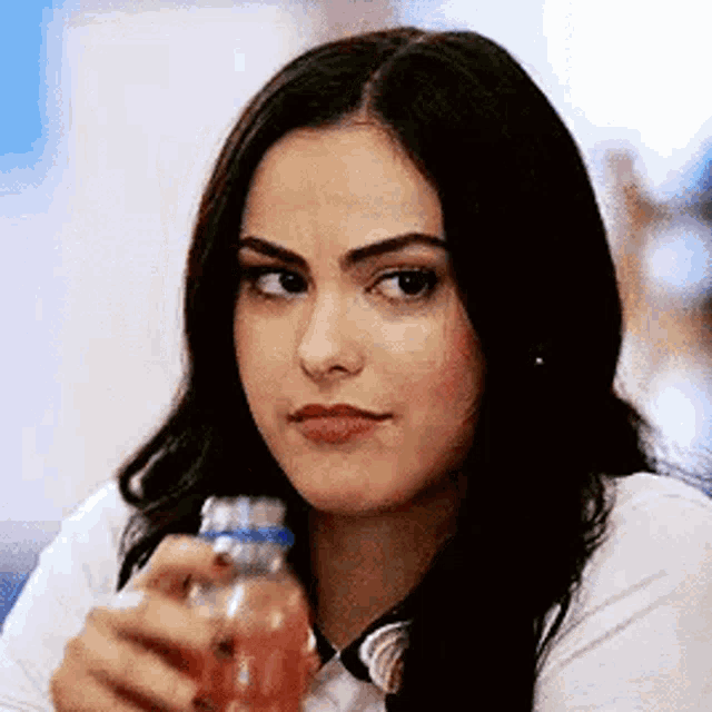 a woman is holding a bottle of orange juice and making a face .