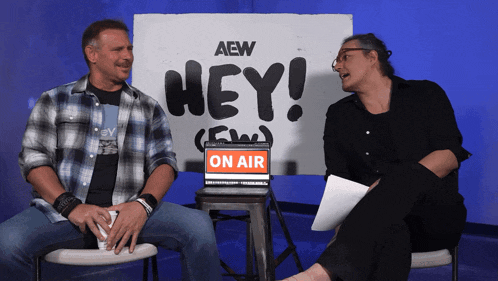 two men sit in front of a sign that says hey on air