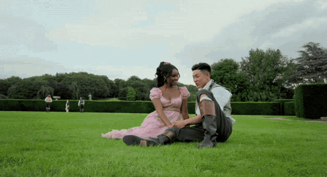 a woman in a pink dress sits on the grass with a man