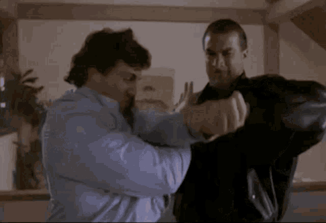 two men are fighting each other in a living room . one of the men is wearing a mask .