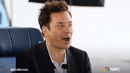 a man in a suit is sitting on a blue couch with a nbc logo behind him