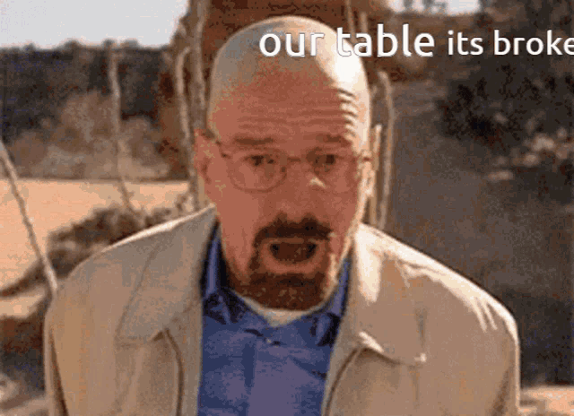 a bald man with glasses and a beard is standing in front of a sign that says our table it 's broke