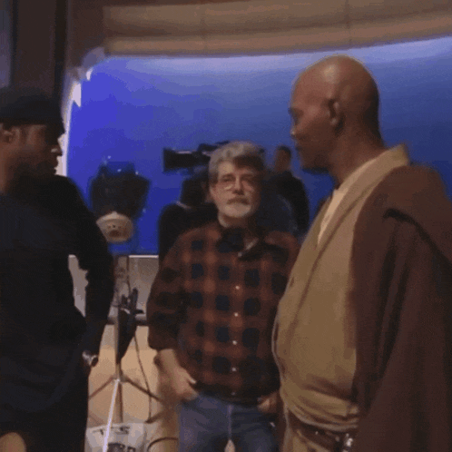 a man in a plaid shirt is talking to another man in a brown robe .