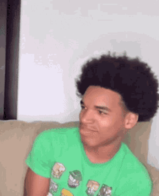 a young man with an afro is sitting on a couch wearing a green shirt