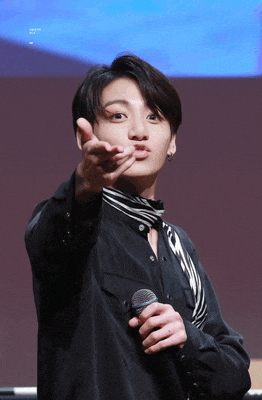 a man in a black shirt is holding a microphone and pointing at the camera