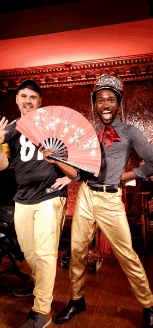 a man in a black shirt with the number 8 on it stands next to another man holding a fan