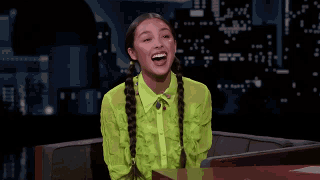 a woman wearing a neon green shirt and braids smiles while sitting at a table