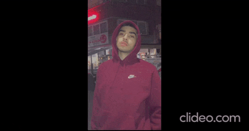 a man in a red hoodie is making a funny face and waving at the camera .