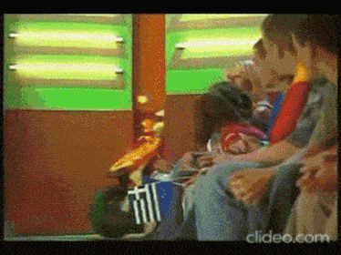 a group of people are sitting in front of a green wall with the words clideo.com on the bottom