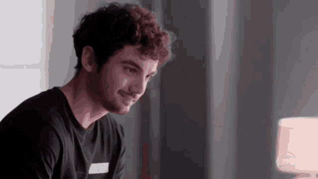 a man with curly hair and a beard is smiling while sitting at a table .