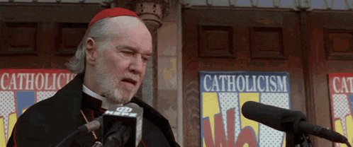 a man speaking into a microphone with a sign behind him that says catholicism