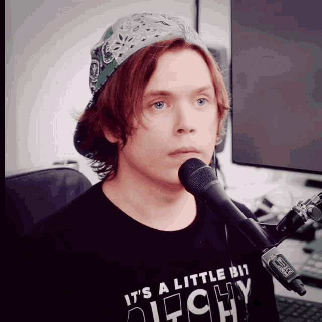 a man wearing a hat and a shirt that says it 's a little bit anarchy is singing into a microphone