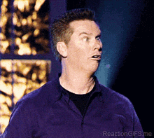 a man in a purple shirt is making a funny face with the words reactiongifs.me below him