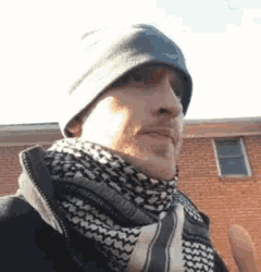 a man wearing a scarf and a hat is giving a middle finger .