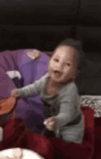 a baby is sitting on a couch with a plate of food in front of him and smiling .