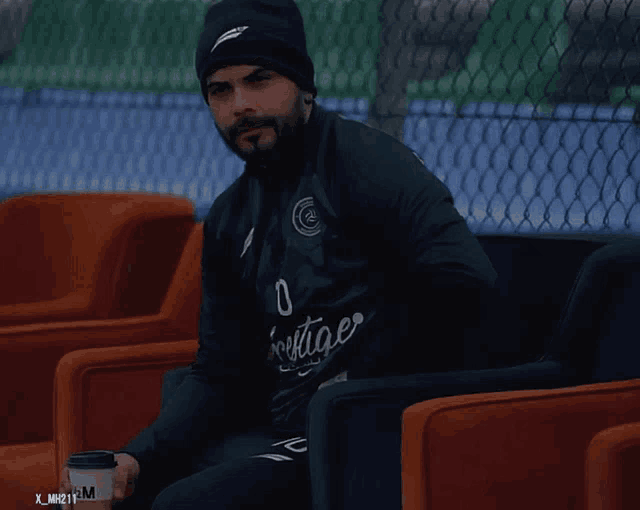 a man wearing a black jacket that says heritage sits in a chair
