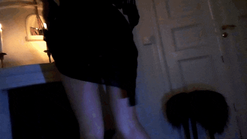 a woman in a black dress is walking through a dark room