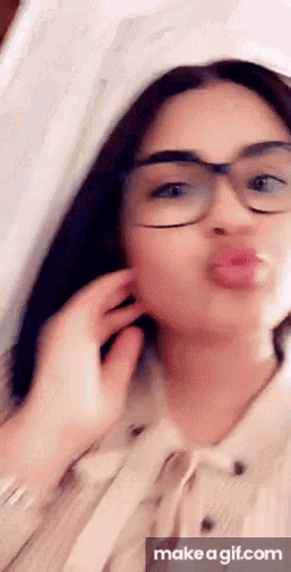 a girl wearing glasses is blowing a kiss