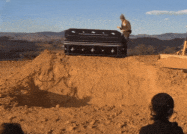 a man standing next to a large black coffin in the dirt