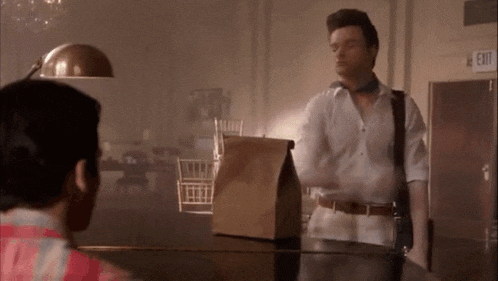 a man in a white shirt is standing next to a brown bag