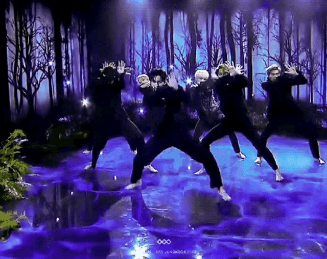 a group of dancers are dancing on a stage in front of a forest .