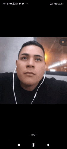 a man wearing ear buds looks at the camera with the time 9:12 pm