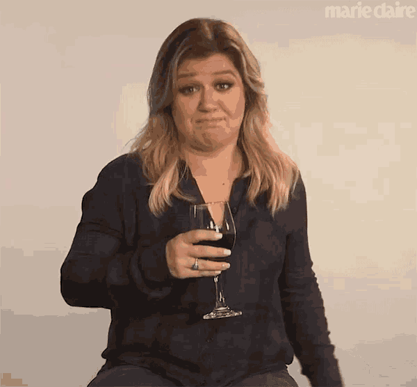 a woman is holding a glass of red wine and making a face .