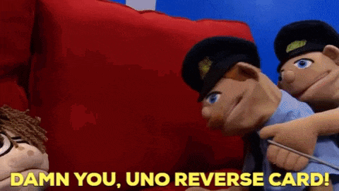 a group of puppets are sitting on a red couch and one of them is pointing at another one .