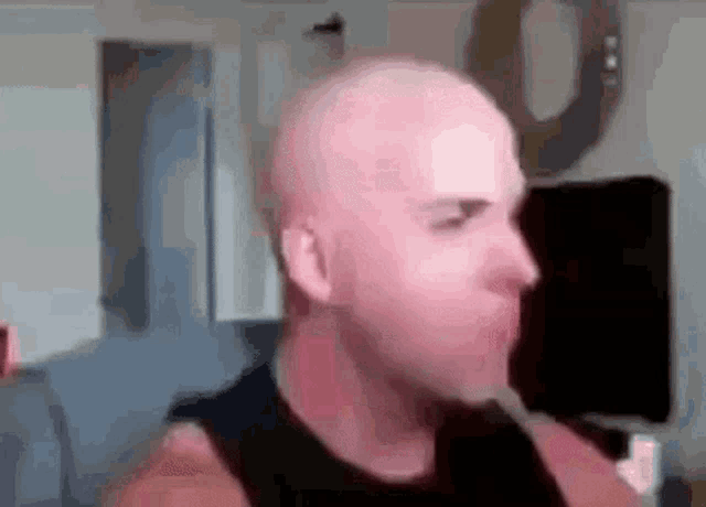a bald man in a black tank top is making a funny face in a living room .