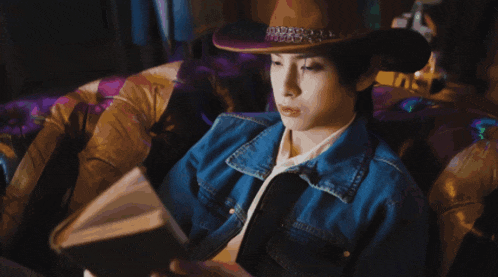 a man wearing a cowboy hat and a denim jacket is sitting on a couch