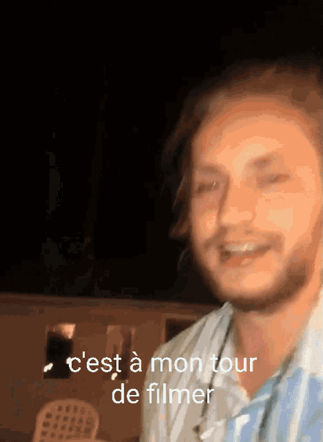 a man with a beard is smiling with the words c'est a mon tour de filmer below him