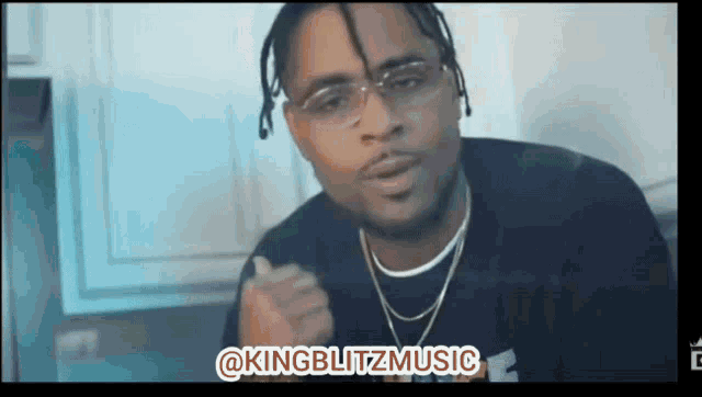 a man wearing glasses and a necklace is giving a thumbs up
