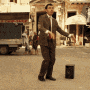 a man in a suit and tie is standing on a sidewalk next to a can .