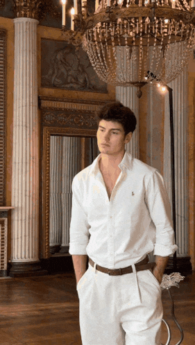 a man in a white shirt and white pants is standing in front of a chandelier